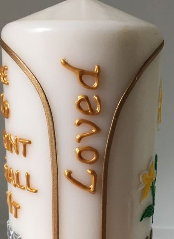 Close-up of gold script reading Forever Loved on the side of a candle