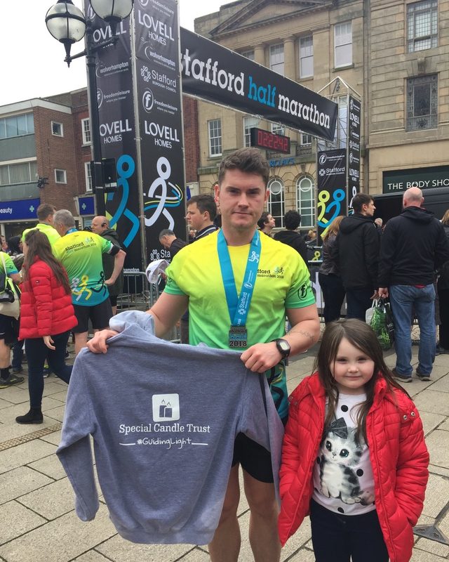 A runner with a Stafford Half Marathon 2018 medal holding a Special Candle Trust hoodie, beside a young girl