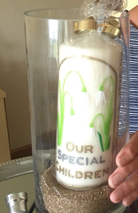 Candle decorated with snowdrops and the words Our Special Children, in a glass vase