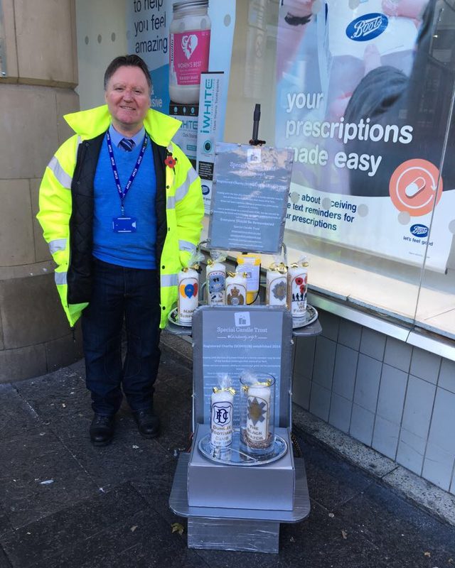 A Special Candle Trust volunteer in a high-visibility jacket beside a street stall of candles